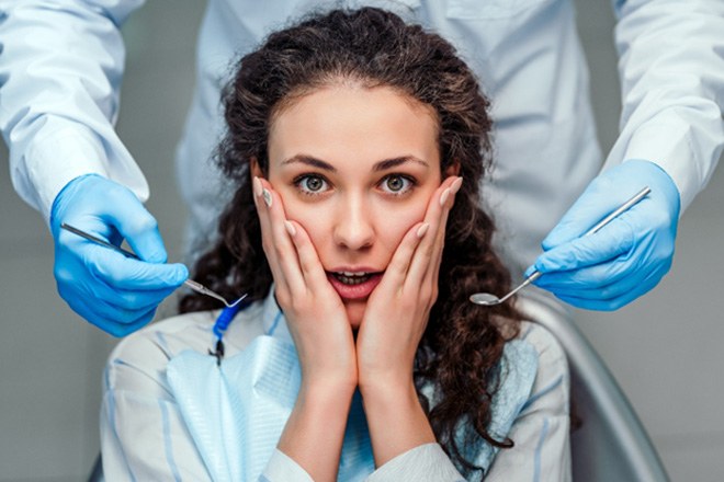 Woman in dental chair holding her cheeks
